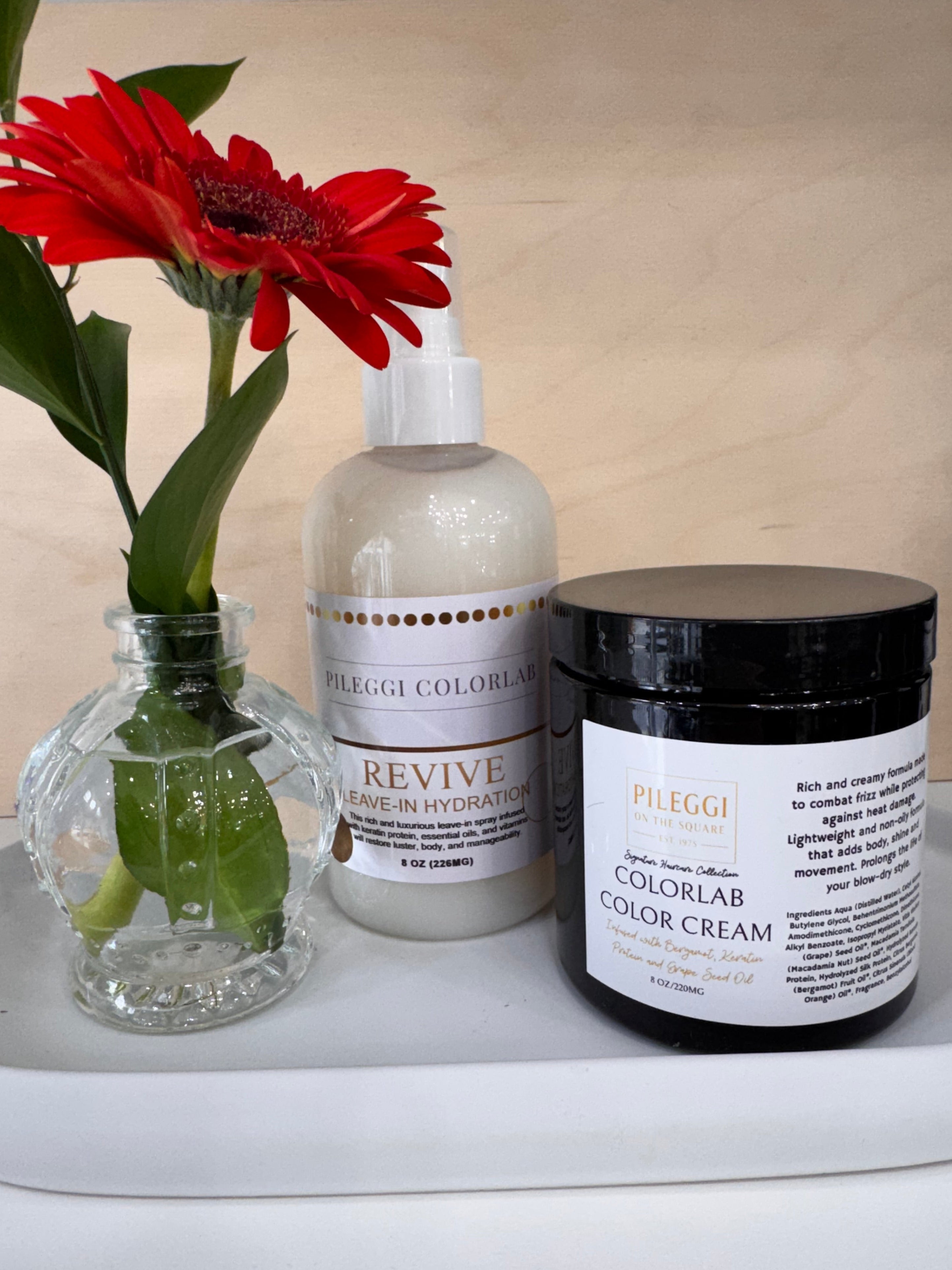 Two HAIR CARE bottles and a red flower on a wooden surface